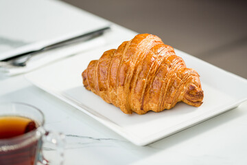 Croissant on a white porcelain plate with tea on the side