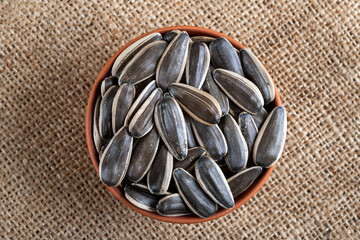 Fototapeta na wymiar Black sunflower seeds in a bowl on burlap sack,top view 