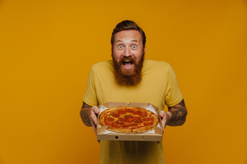 Happy man in t-shirt smiling and holding pizza while standing isolated