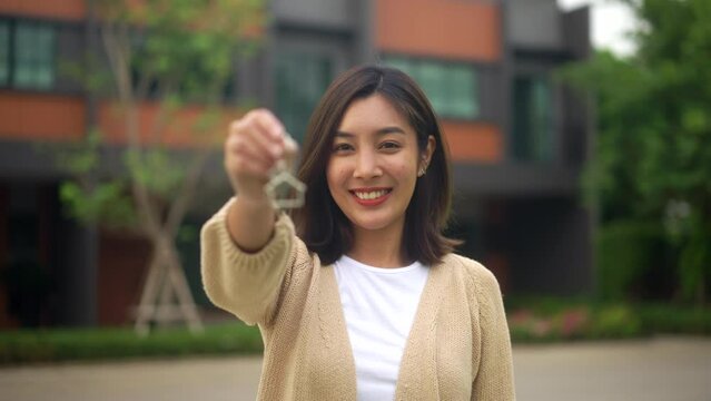 Happy feeling of woman buying or rent new home she holding key front of new house. Surprised happy young asian woman and smile to renter or purchase apartment, home. Moving day relocation concept.