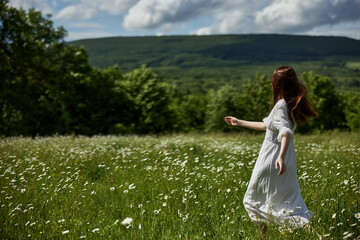 Fototapeta na wymiar a free woman in a light dress runs through a field of daisies with her back to the camera