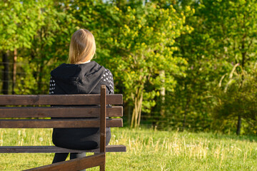 Dziewczyna siedzącą samotnie na brzegu ławki parku w pogodny dzień  - obrazy, fototapety, plakaty