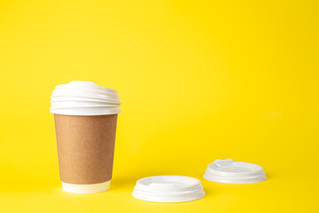 Paper cup and plastic lids on a yellow background isolated.
