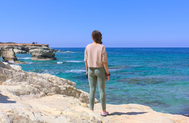 A woman enjoying the beautiful view of the bay and ATV quads in the distance on a sunny day. Paphos, Cyprus near the Edro III shipwreck.