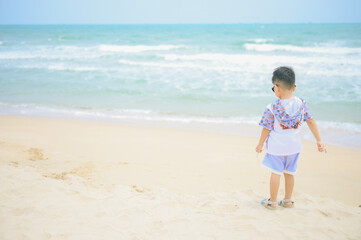 Fototapeta na wymiar Asian boy wearing sunglasses is playing on a sandy beach near the sea.