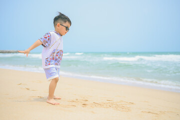 Fototapeta na wymiar Asian boy wearing sunglasses is playing on a sandy beach near the sea.