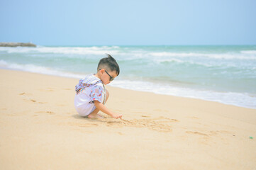 Asian boy wearing sunglasses is playing on a sandy beach near the sea.