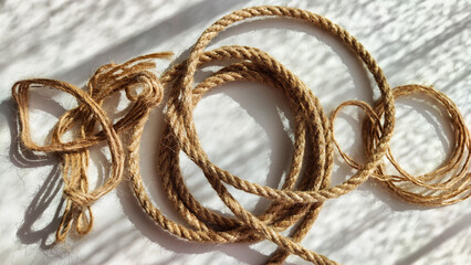 Jute twisted rope lying on a white surface with shadows from the sun. Abstract background, texture, pattern, frame © keleny