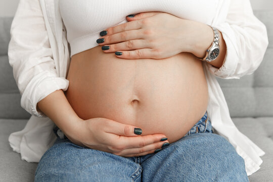 Cropped image pregnant woman sitting in appartment strokes hugging the belly tummy abdomen enjoying pregnancy. Future family, baby infant expecting child inside

