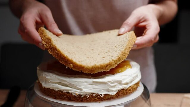 The pastry chef assembles the cake, placing a layer of sponge cake on top of the orange compote filling, in slow motion.