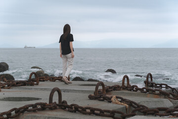 大きな鎖で繋がれた波消しブロックを歩く女性 三保松原海岸 - obrazy, fototapety, plakaty