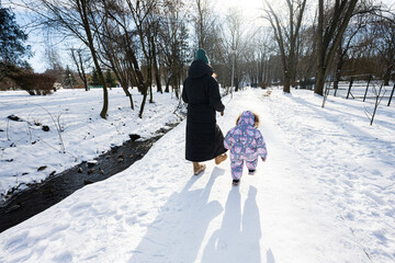Back view of mother and child walking on a sunny frosty winter day in the park.