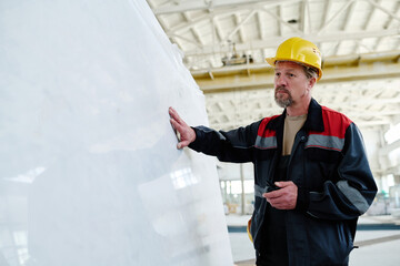 Engineer in uniform examining the structure of marble before production while standing in workshop