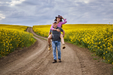 Fototapeta premium Farmers doing a piggyback ride through canola field