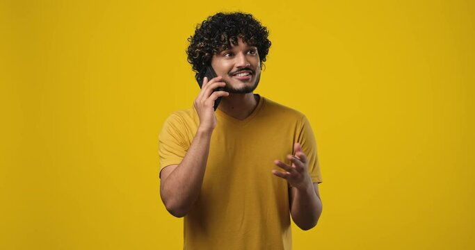 Young smiling indian man talking on the phone answering phone call over yellow orange background