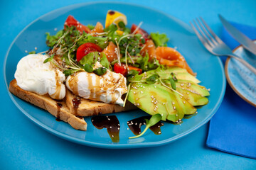 Healthy breakfast. Avocado and salmon, poached egg and toast, salad and vegetables. Microgreens on a plate. Food bowl. Lunch on a blue plate. Sauce and sesame seeds, lemon tomatoes. Top view.