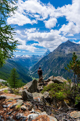 Travelling in Switzerland, a man with backpack standing on the rock looking at Matterhorn mountain view. Trekking in Zermatt, Switzerland - obrazy, fototapety, plakaty