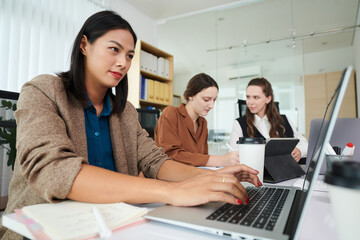 Businesswoman answering e-mails when colleague discussing document in background