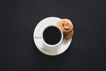 Cup of coffee and cookies on a black background, top view.