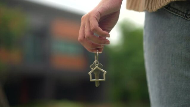 Close up shot of hand holding key woman buying or rent new home walking to new house. First time to renter or purchase apartment, home. Moving day relocate concept.