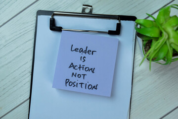 Concept of Leader is Action Not Position write on sticky notes isolated on Wooden Table.