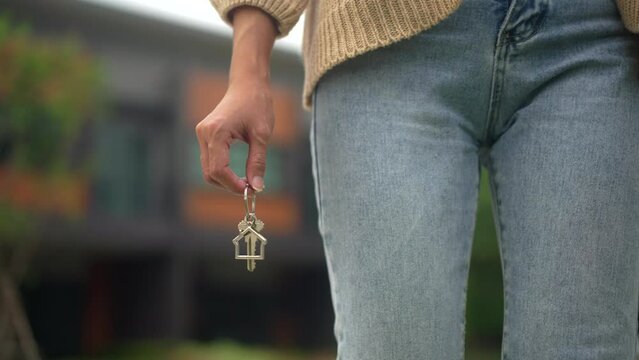 Close up shot of hand holding key woman buying or rent new home walking to new house. First time to renter or purchase apartment, home. Moving day relocate concept.