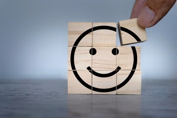 Hand placing wooden cube with smiley icon. Mental health, wellness and healthy mind concept