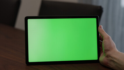 Man at home using tablet pc with green screen while sitting at the table