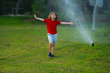 Cute little kid play in garden at summer day. Child enjoy summer in backyard. Little boy having fun running under water spraying sprinkler. Watering summer grass. Summer holiday for kids.