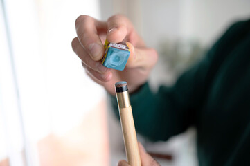 A billiard player prepares to play by putting blue chalk on his cue. Details of the game of billiards