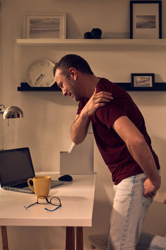 Man with shoulder and neck pain while working on a laptop at home.