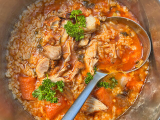 Chicken soup with rice and vegetables in a pot with large spoon Home cooking pov
