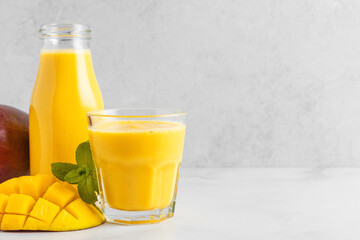 Mango smoothie in bottle and glass with fresh fruits. Summer tropical drink on white background