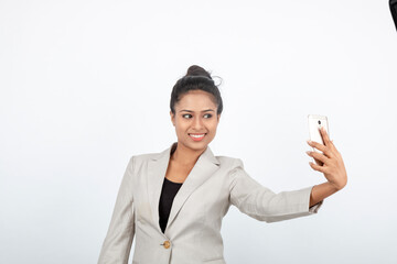Corporate office lady with black hair having playful moment with pen, smart phone in formal wear wearing white blazer against white background.