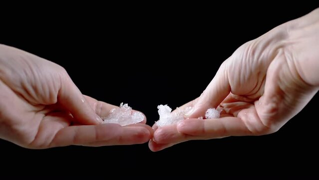 Close up, Woman Holding Melting Wet Snow in her Hands on a Black Background. Snow crystals, ice melt, and scatter around. Explosion. Isolated background. Part of. Hands. Unrecognizable person. Winter.
