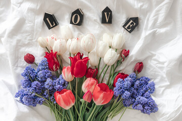 A bouquet of fresh flowers and a decorative word Love in a white bed, top view.