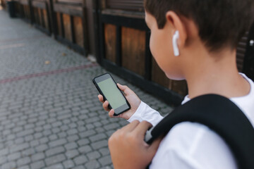 Obraz na płótnie Canvas Mock up of teenage boy with wireless headphones use phone otside. Green screen