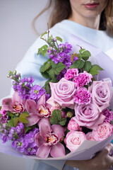 Woman florist with a bouquet of pink orchids and roses with raspberry branches. European bouquet of mixed flowers. Flower shop. Master classes and floristry courses. Flower delivery.