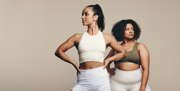 Two fit young women stand together in sportswear, embracing a healthy lifestyle in the studio