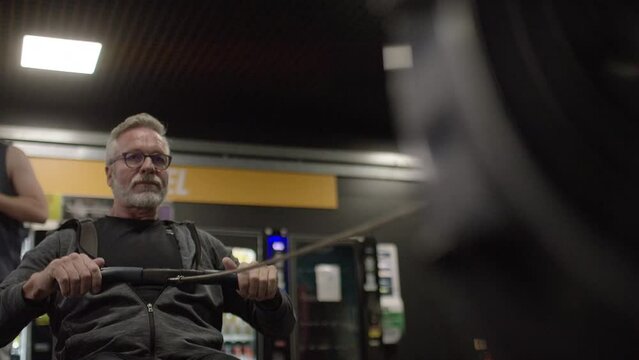 Senior male in his 60s working out on a rowing machine, in slow motion 