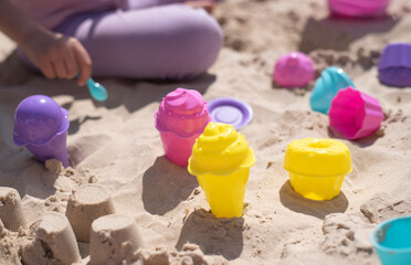 Child play in stand with pink and yellow molds of ice cream for sand. Summer time  joy and play in sand outdoor. Great vacation with children.