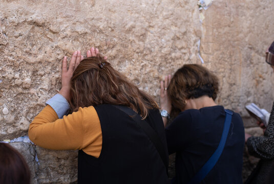 Two religion different races women standing by back and praying on Western Wall. notes of paper written prayers placing in cracks. old part of Jerusalem city. tourism in Israel
