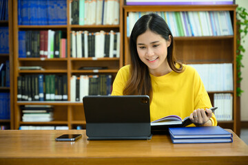Smiling female university student doing research on digital tablet, learning lessons, preparing for exams in library
