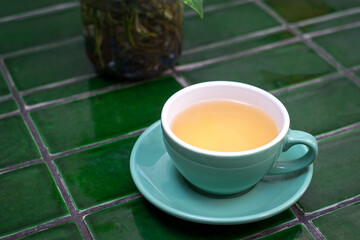 Hot Chamomile tea in a green cup on green tiled table.