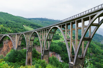 The old bridge between the mountain river. Against the background of mountain peaks in summer.