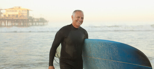 Older surfer carrying board on beach