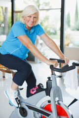 Obraz premium Older woman riding exercise bike in home