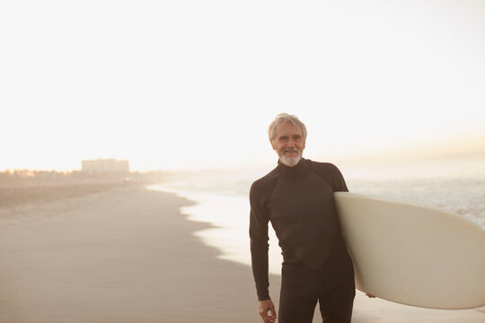 Older surfer carrying board on beach