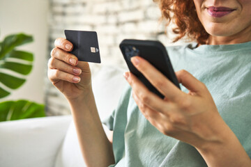 Young redhair woman sitting on her sofa doing online shopping on laptop in morning light