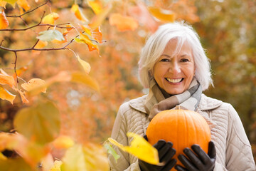 Older woman holding pumpkin in park